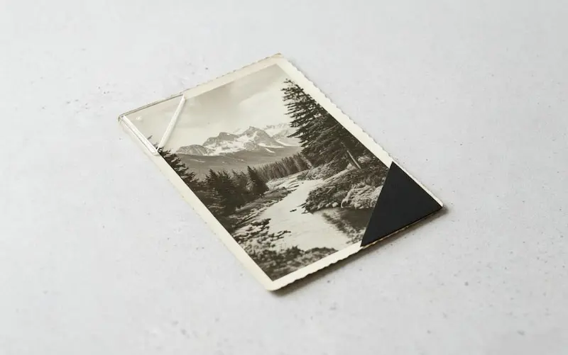 A close-up comparison of a clear polypropylene corner and a black paper corner applied to the same vintage photograph to show material differences.